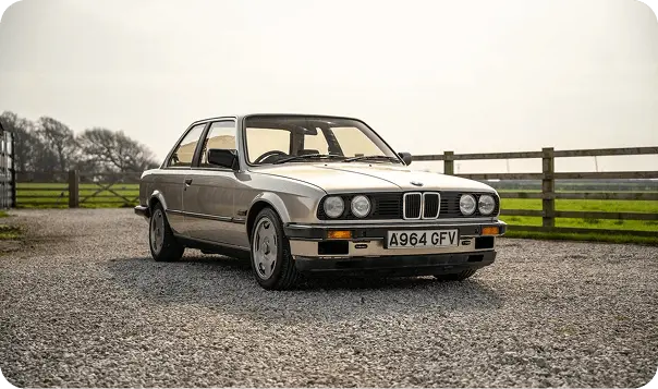 Gold 1983 BMW E30 316 parked on a gravel driveway